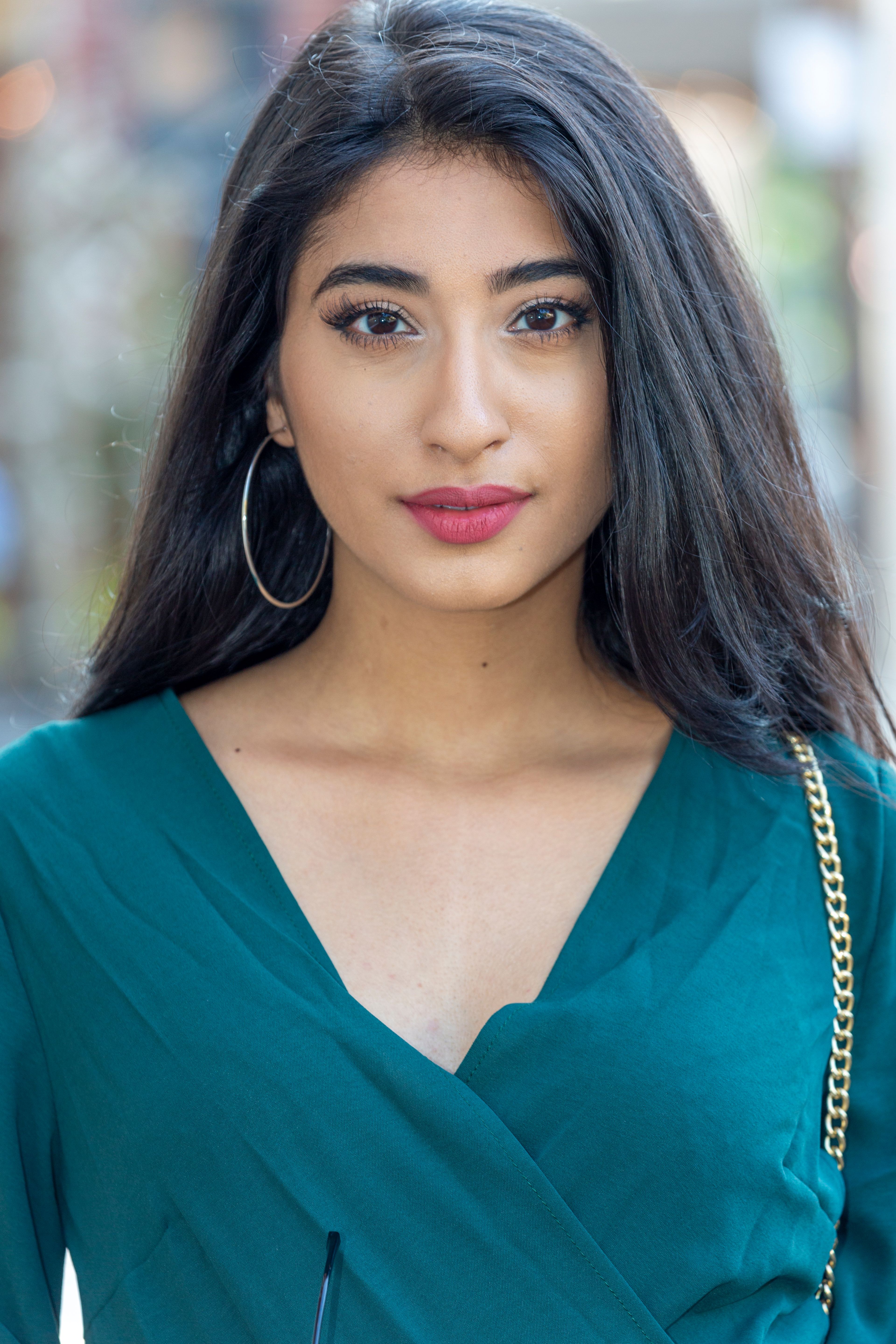 Portrait of a stylish young woman in a teal dress outdoors, showcasing elegance and confidence.