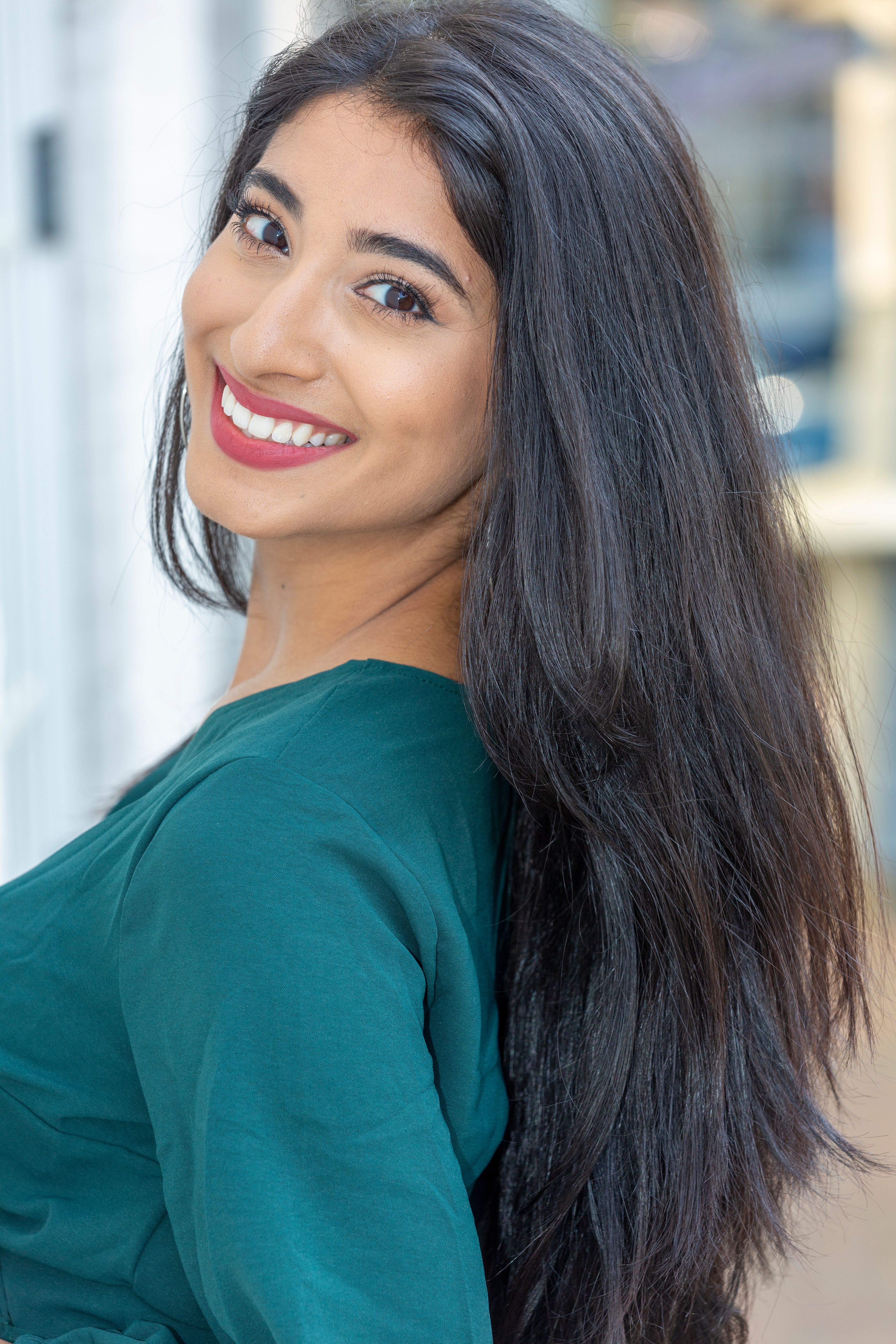 Portrait of a smiling woman with long dark hair and green top, looking over shoulder.