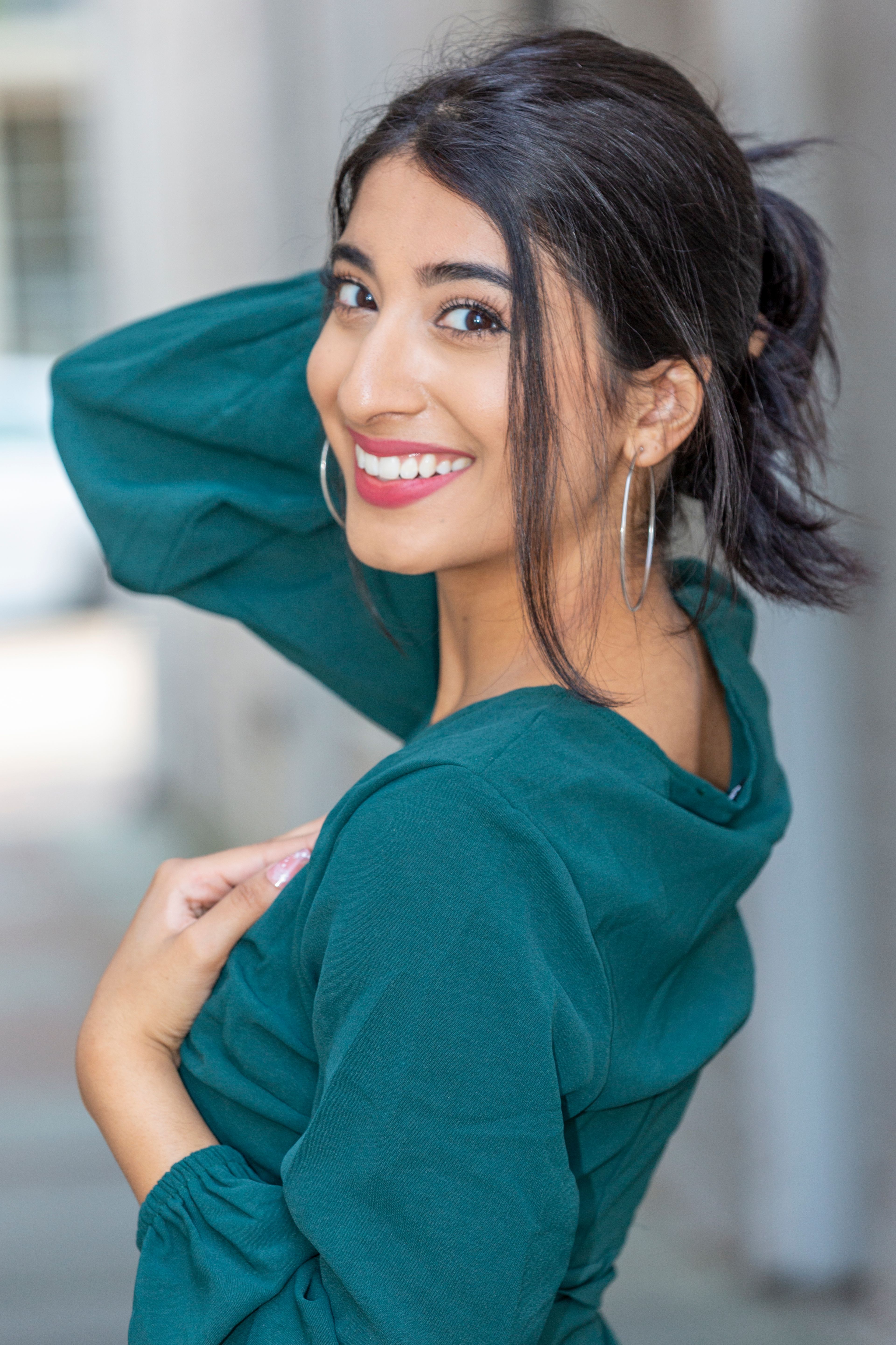 Portrait of a smiling woman posing with hoop earrings and green dress, radiating confidence and style.