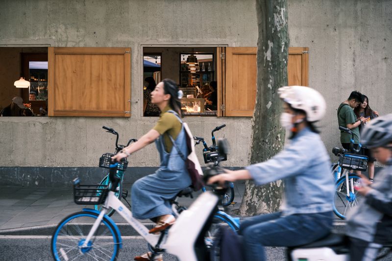 Group of people riding bicycles past a cafe. Urban afternoon scene with open windows.