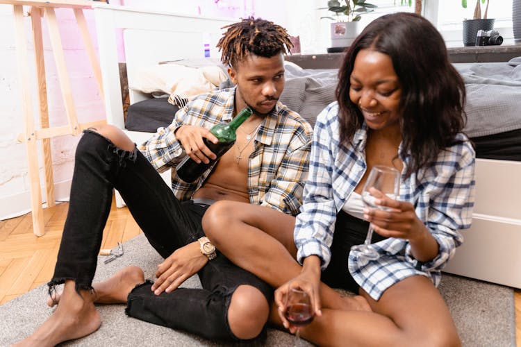 A Couple Sitting On The Floor Drinking Wine