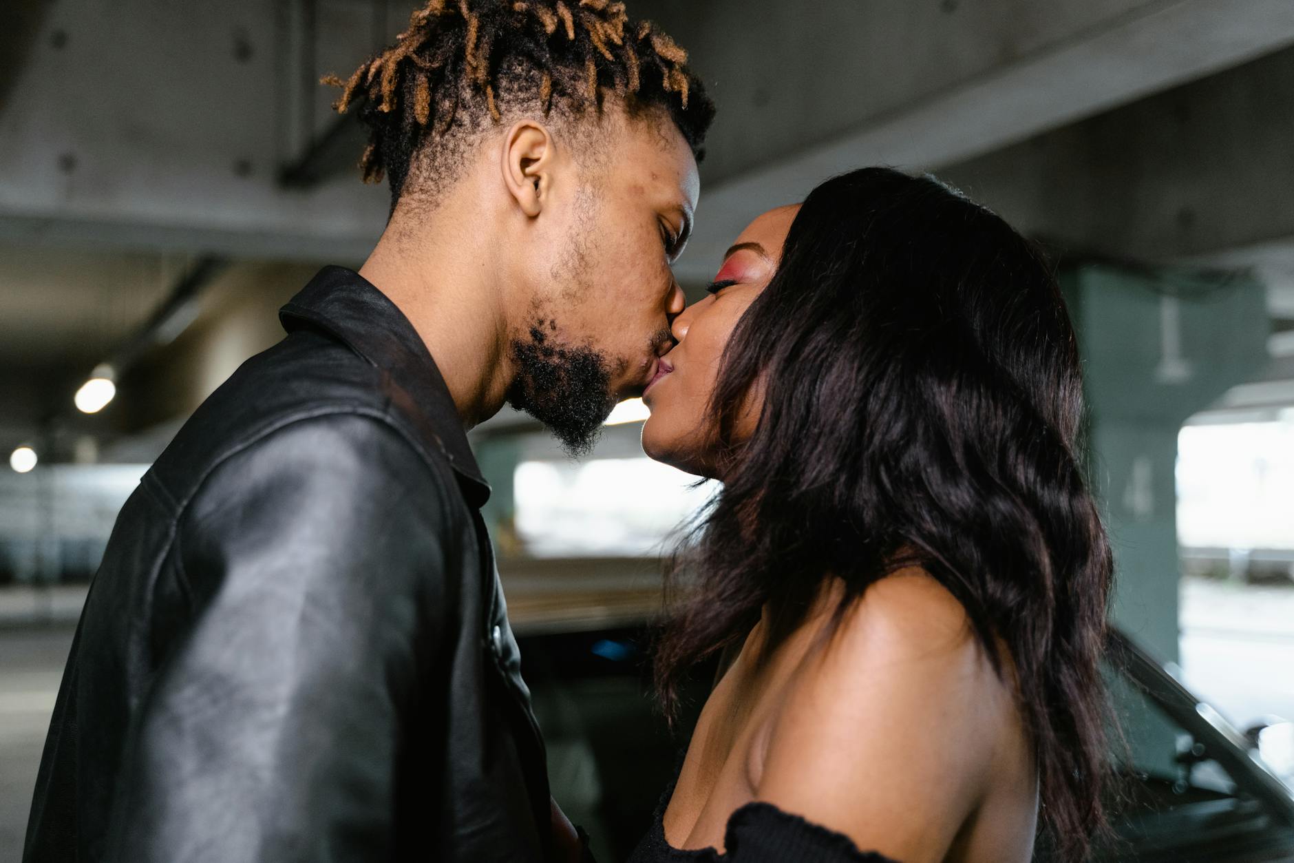 A close-up of an interracial couple sharing an intimate moment and kiss indoors.