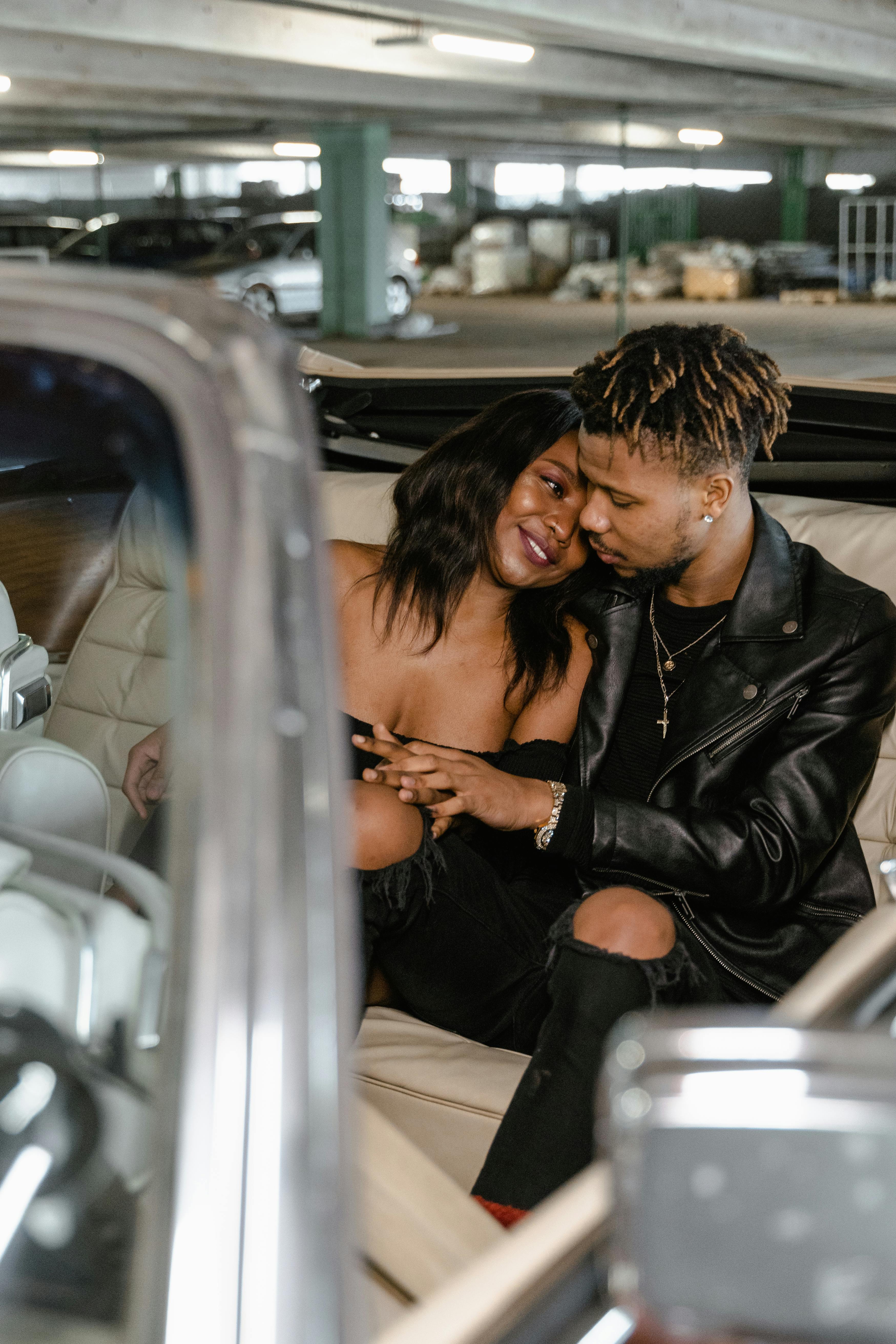 a couple sitting inside the car in a parking area of a building