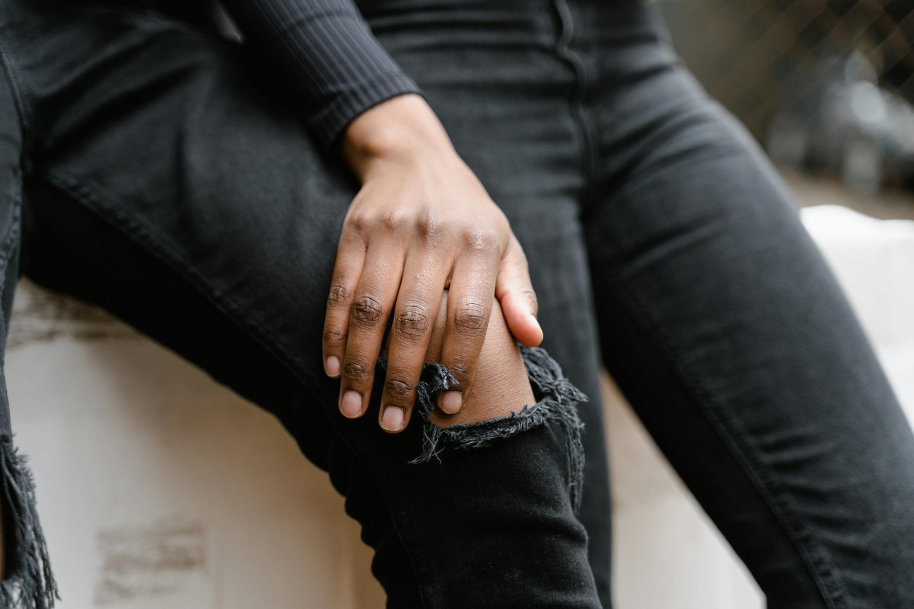 A close-up view of a hand resting on the knee of ripped black jeans, showcasing casual style.