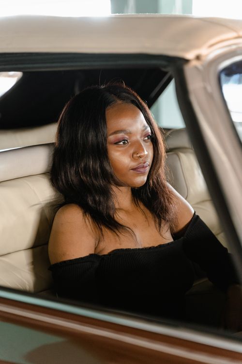 Free A woman elegantly posed in a car, wearing an off-shoulder black top, exuding poise and style. Stock Photo