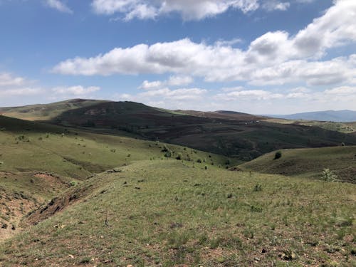 Green Mountains and Field Under a Blue Sky with White Clouds