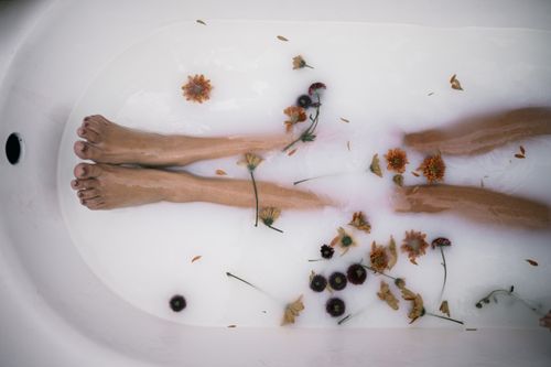Free A serene bath scene showcasing legs submerged in milky water with floating flowers, emphasizing relaxation and self-care. Stock Photo