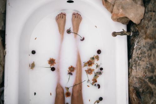 Free Top view of a woman's bare legs in a bathtub filled with milk and scattered flowers for a soothing bath experience. Stock Photo