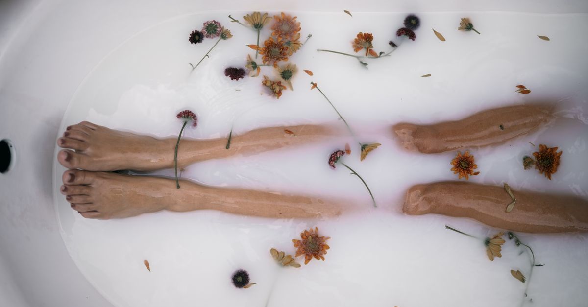 Serene bath scene with submerged legs and scattered flowers, creating a tranquil atmosphere.