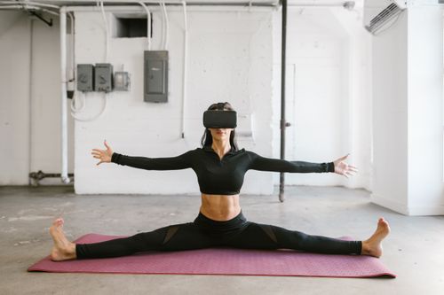 Free A woman stretches on a yoga mat while wearing a virtual reality headset, indoors. Stock Photo