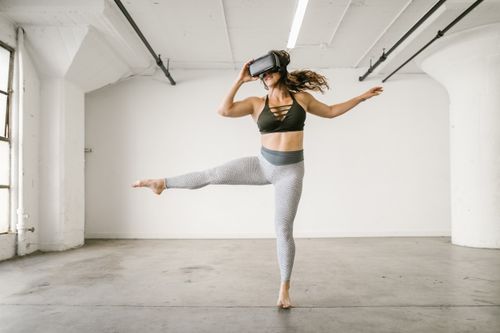 Free Woman in athletic attire explores virtual reality using a VR headset while dancing in a modern studio. Stock Photo
