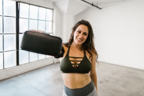 Free Smiling woman in gym attire holding a VR headset in a bright room. Stock Photo