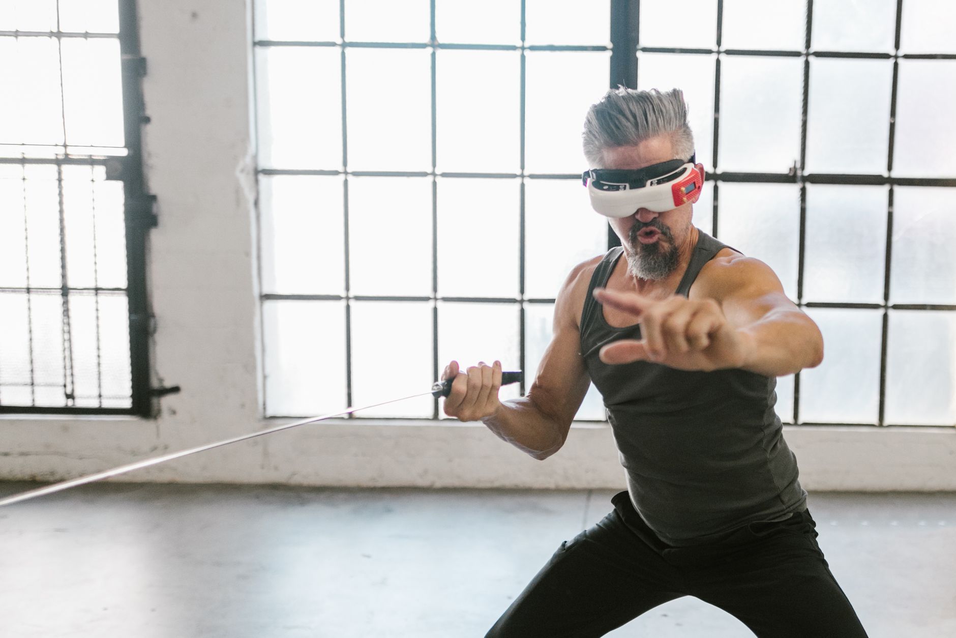 Adult man engaging in virtual training with a VR headset and sword indoors, showcasing future technology.