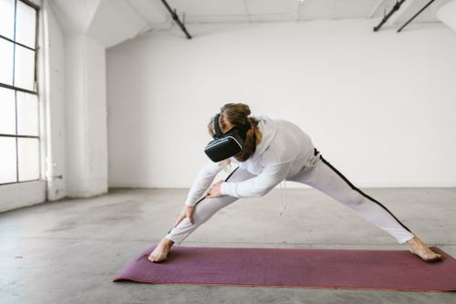 Free A woman in sportswear stretches on a yoga mat using a virtual reality headset indoors. Stock Photo