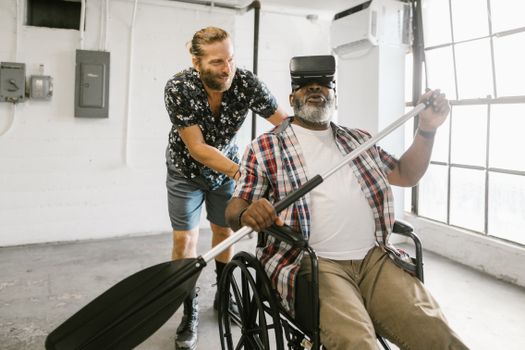 Two men enjoying virtual reality; one is in a wheelchair experiencing a rowing simulation.