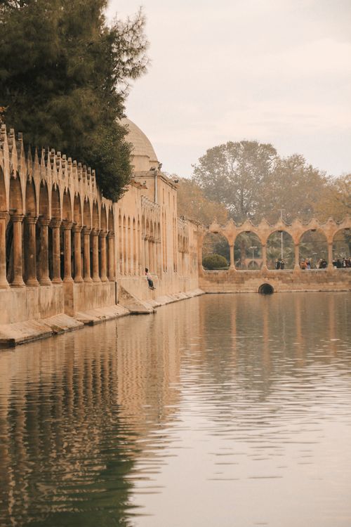 Free A serene view of historic architectural arches reflected in a calm lake, creating a peaceful ambiance. Stock Photo