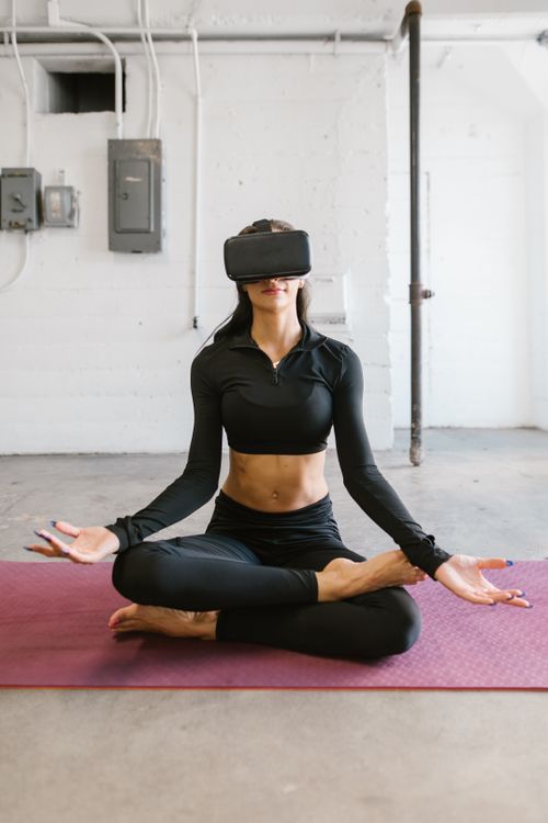 Free Woman in black activewear meditating in a lotus position with virtual reality headset in an industrial studio. Stock Photo