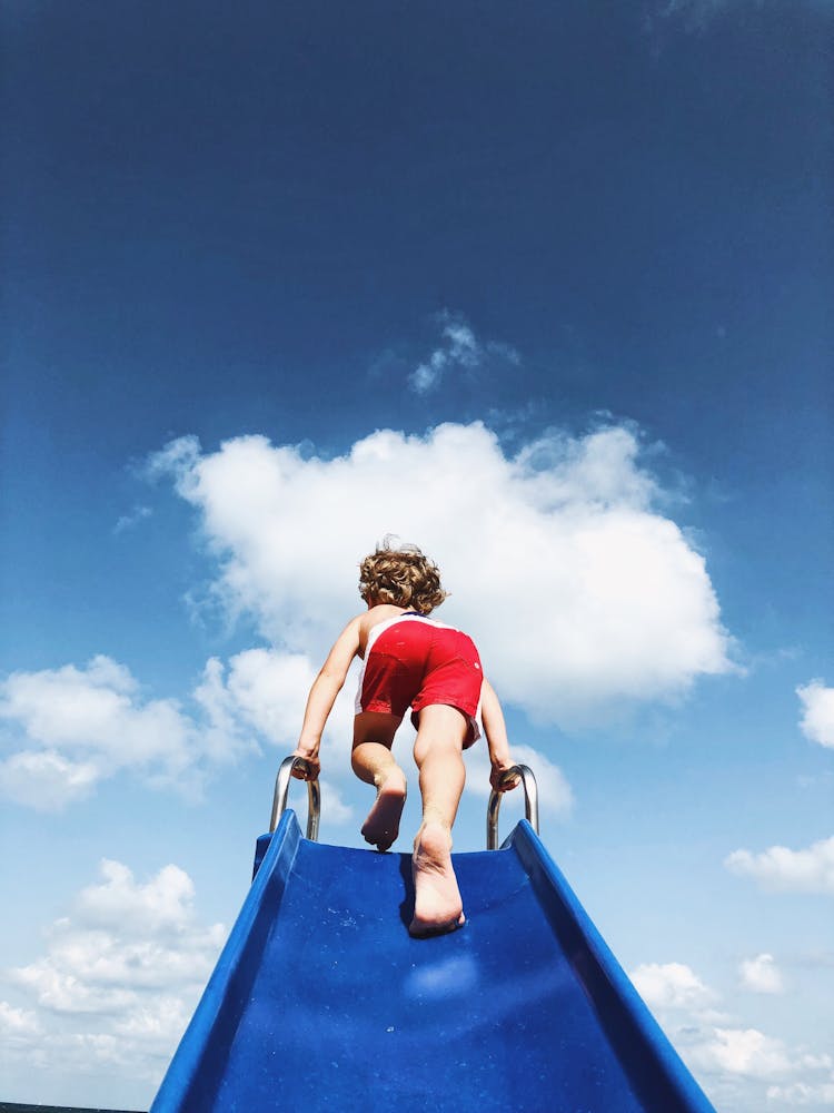 Child Climbing Slide Against Blue Sky