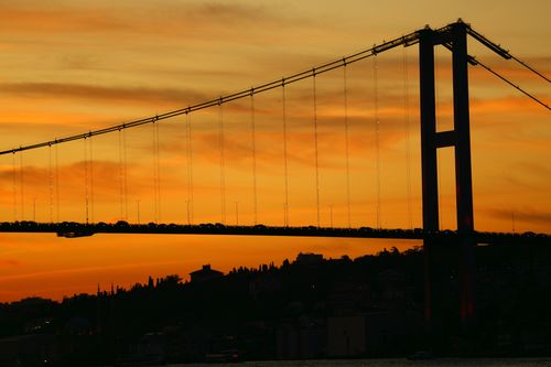 Free Dramatic silhouette of a suspension bridge against a vibrant orange sunset sky. Stock Photo