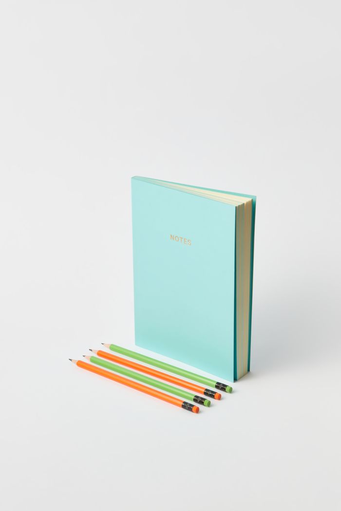A mint notebook with coloured pencils on a white desk