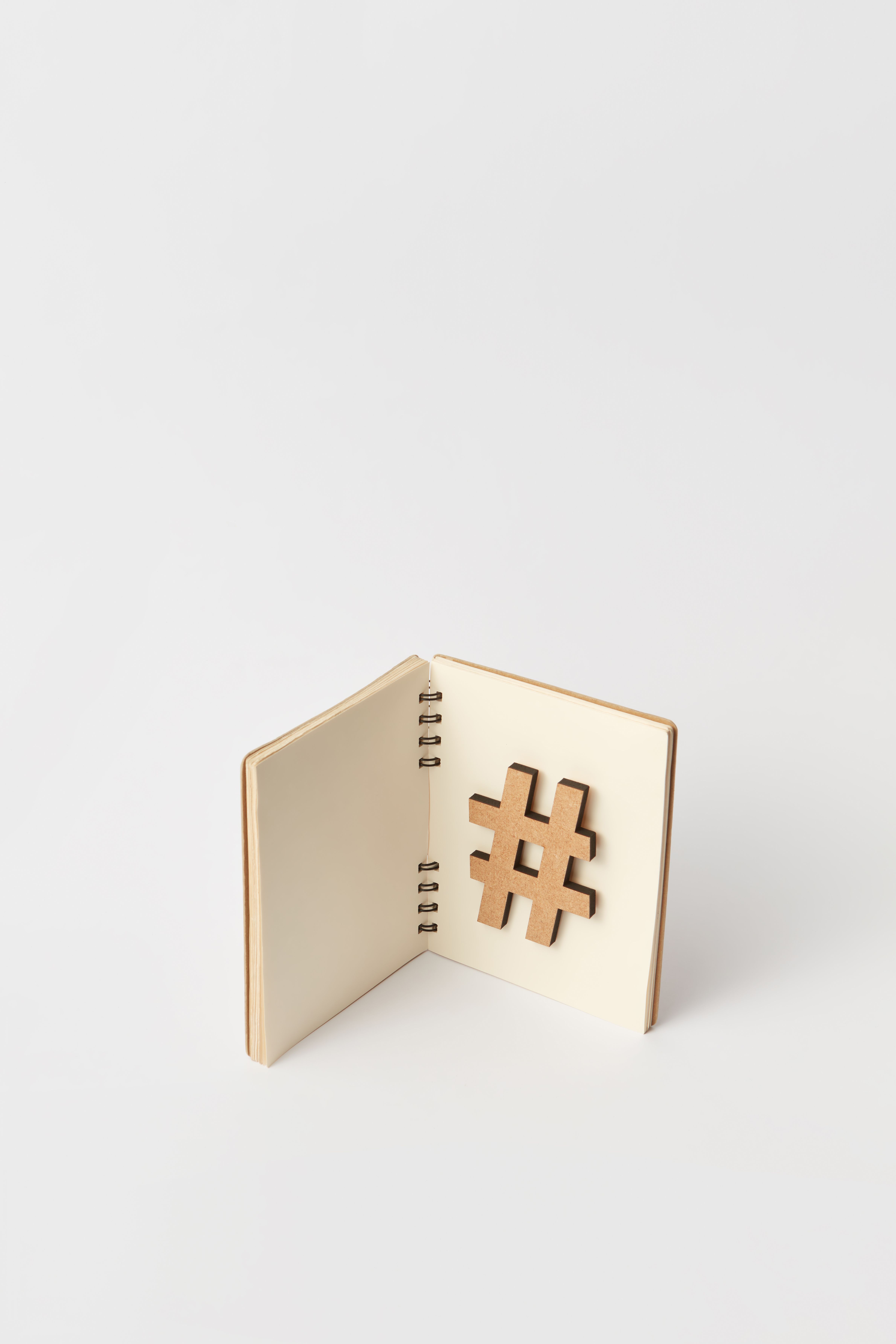 Open notebook with a wooden hashtag symbol against a plain background.