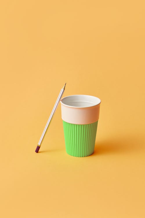 A White Pencil Beside a Green and White Paper Cup