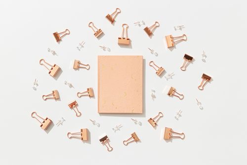 Free A minimalist flat lay of copper binder clips, push pins, and a notebook on a white background. Stock Photo