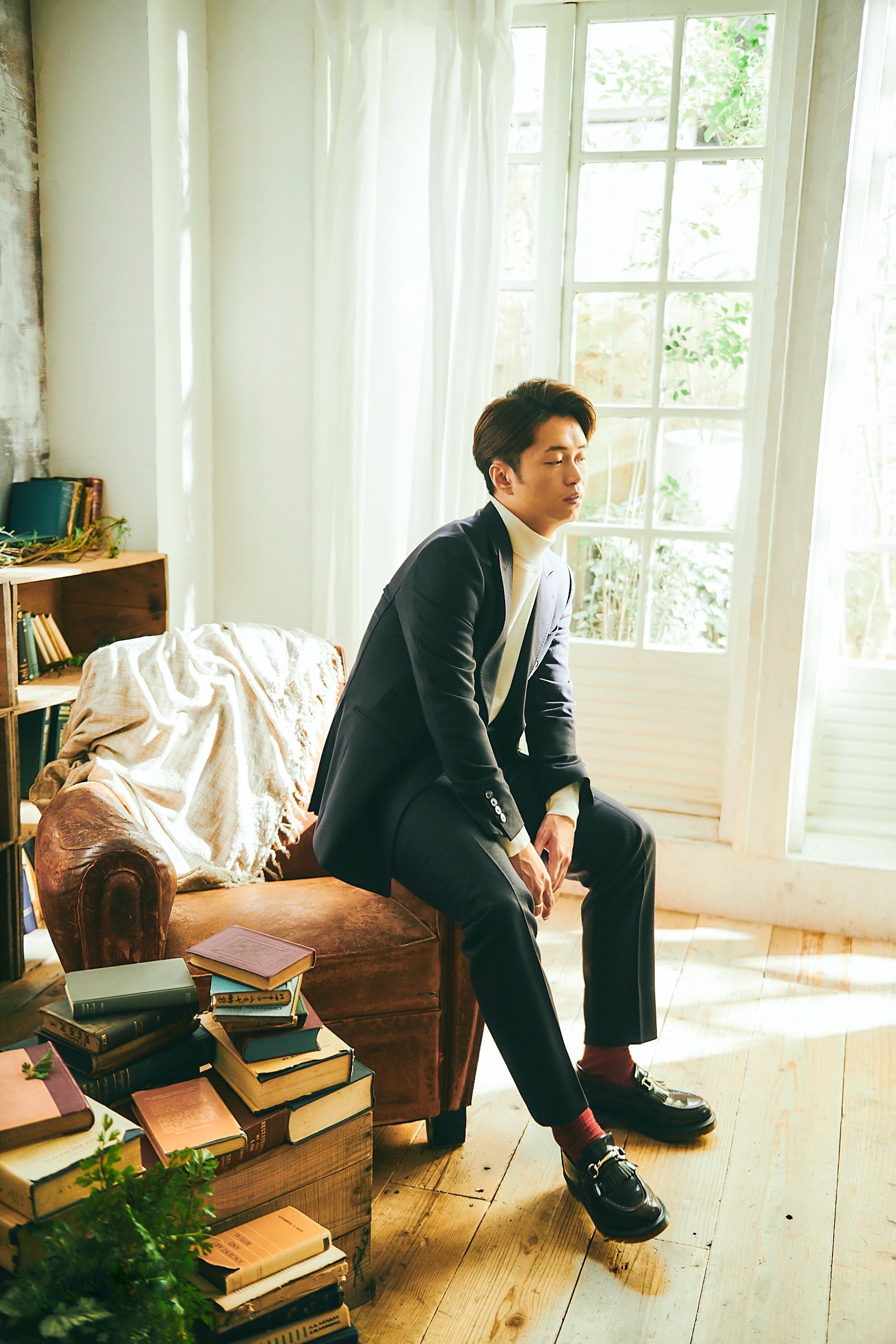 Stylish man sitting in sunlit living room with books, exuding calm and elegance.