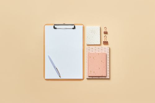 Free Flat lay of a clipboard, notepad, pen, and paper clips on a beige backdrop with copy space. Stock Photo