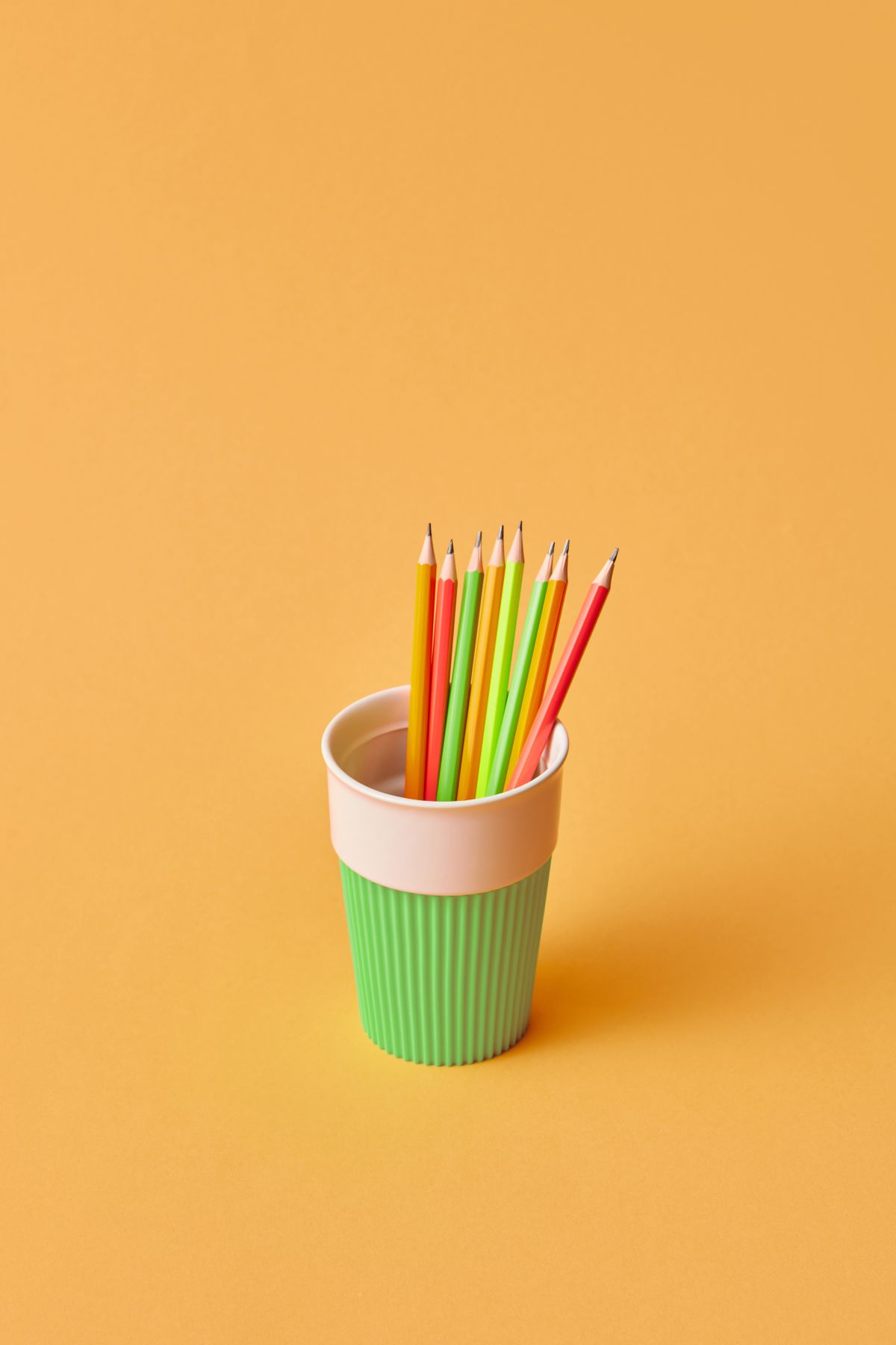 Colored pencils standing in a bright green cup on a desk