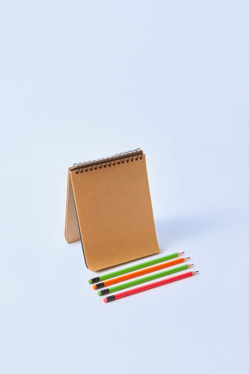 Free Vertical shot of a notepad with colored pencils on a white background, ideal for creative design. Stock Photo