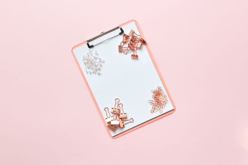 Free Flat lay image of a pink clipboard with binder clips and paperclips on a pastel pink background. Stock Photo