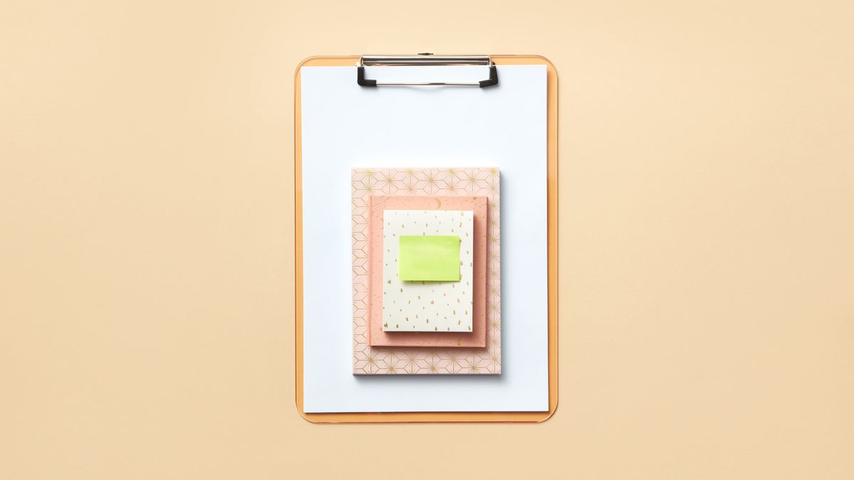 Stylish flat lay of a clipboard with pastel notebooks and a green sticky note on a beige background.