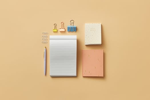 A minimalist flat lay of office supplies on a beige background, including notepads and clips.