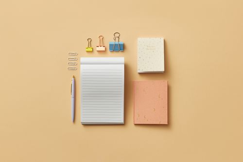 Free A minimalist flat lay of office supplies on a beige background, including notepads and clips. Stock Photo