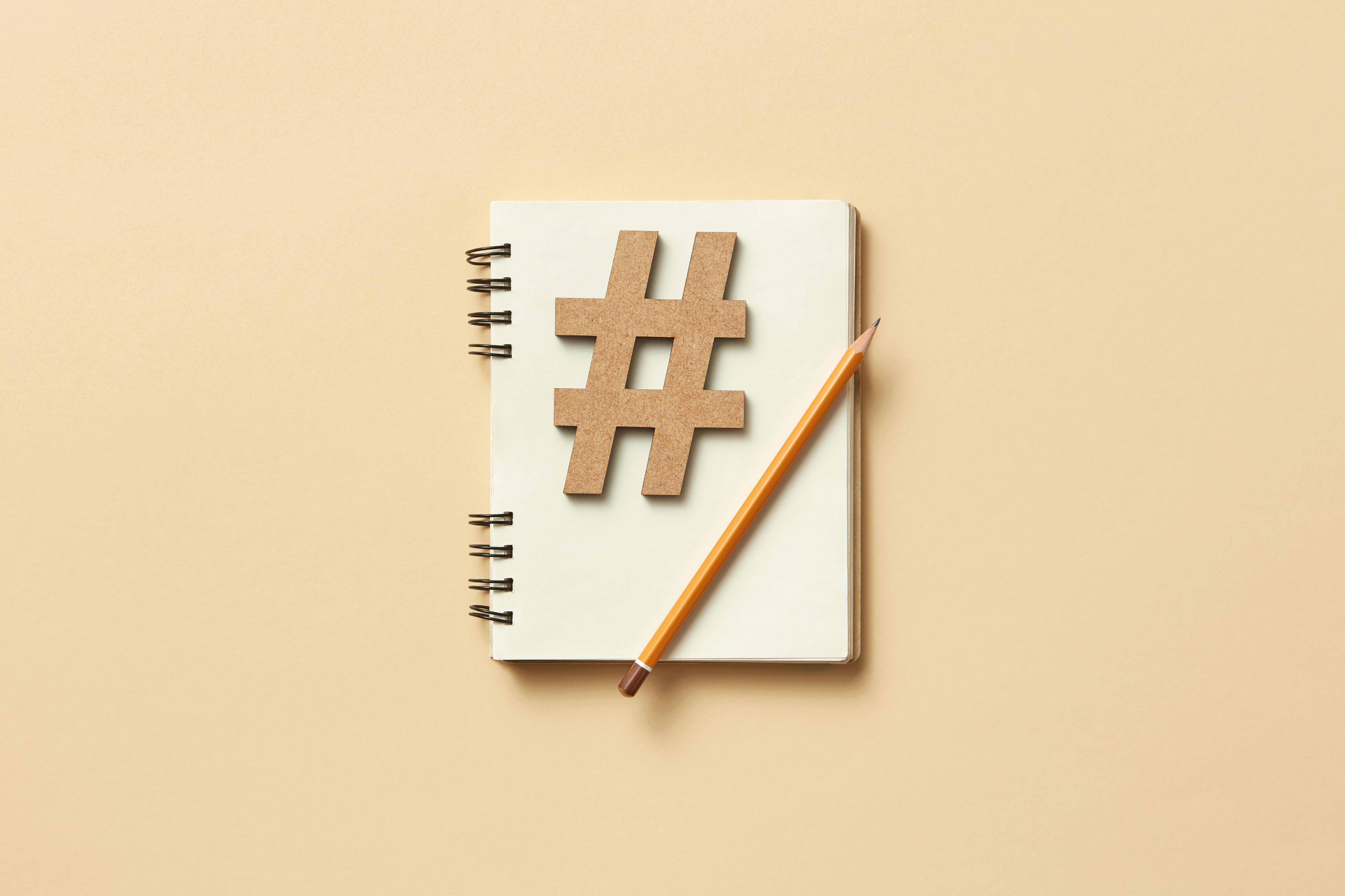 Minimalist flat lay featuring a notebook, hashtag symbol, and pencil on beige background.