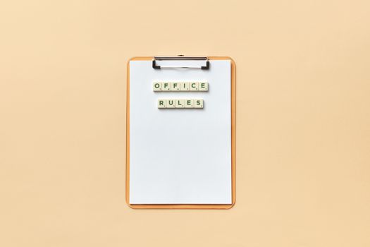 A clipboard with the phrase 'Office Rules' spelled out using Scrabble tiles on a beige background.