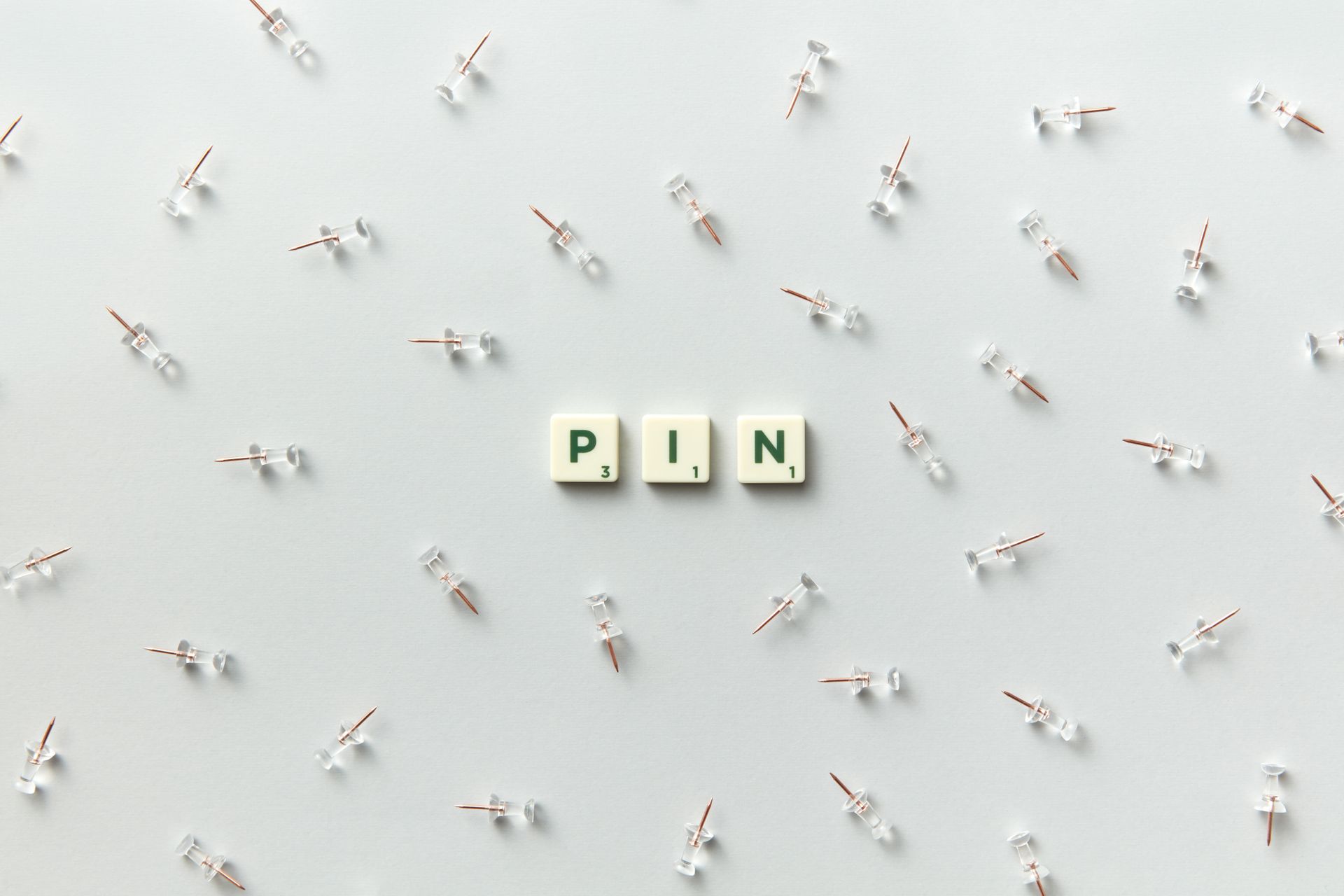 Minimalist arrangement of push pins and scrabble letters spelling 'PIN' on a white background.