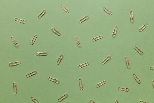 Aesthetic flatlay of scattered gold paper clips on a green background.