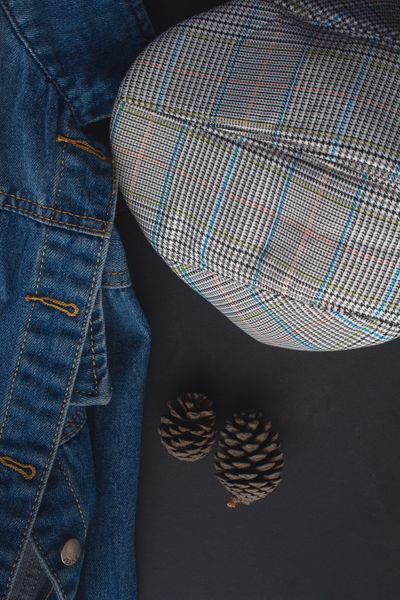 Denim jacket and checked flat cap on a dark surface — photo by Namukolo Siyumbwa on Pexels