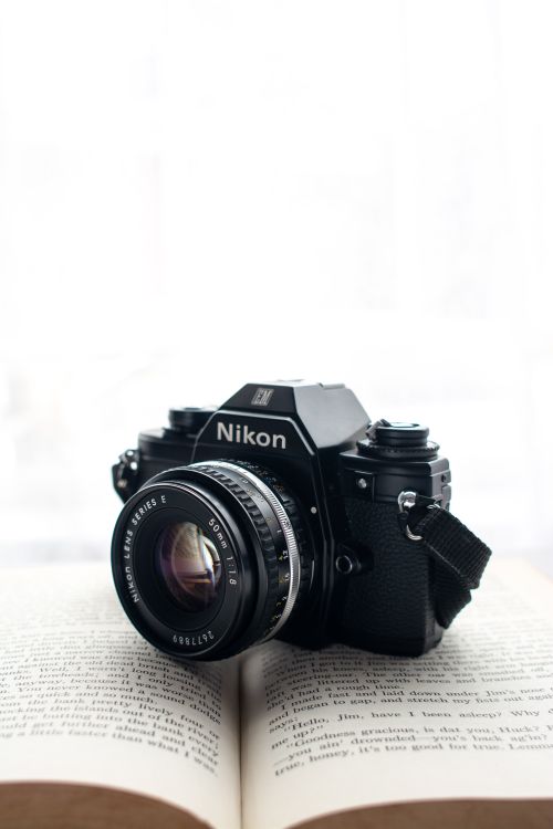 Free Classic Nikon camera resting on an open book with lens detail. Stock Photo