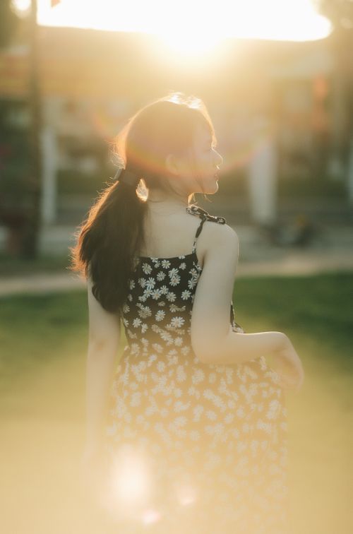 Free A woman in a floral dress captured from behind, bathed in warm sunlight outdoors. Stock Photo