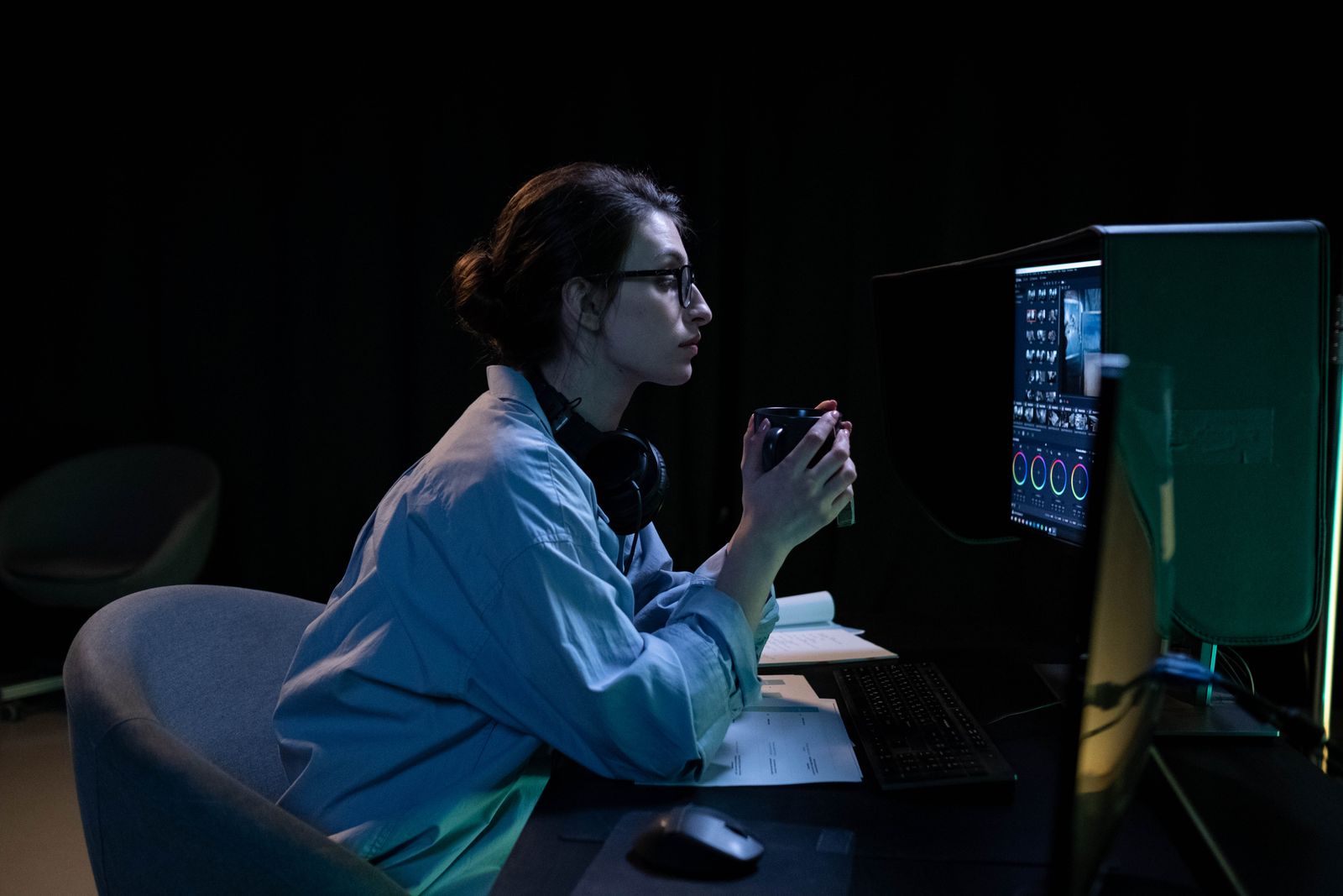 A woman in a dimly lit room working intently on a computer while holding a mug