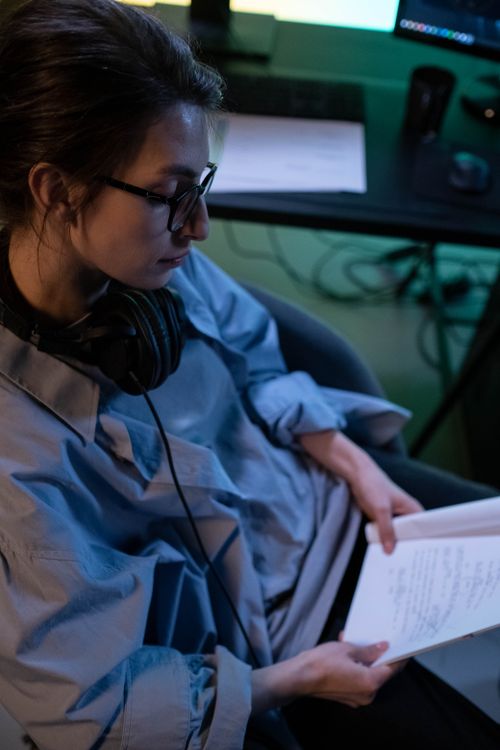 Free Woman wearing glasses and headphones reading documents, sitting in an office environment. Stock Photo