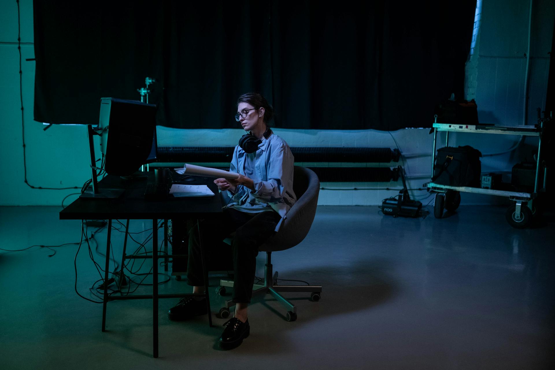 Woman working late in a moody studio environment, concentrating on computer tasks.