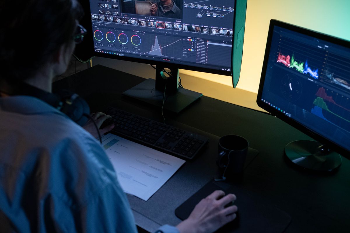A video editor working at a multi-monitor workstation in a dimly lit studio
