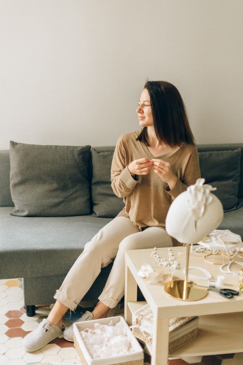 Free Woman sitting on a couch making jewelry in a bright living room. Stock Photo