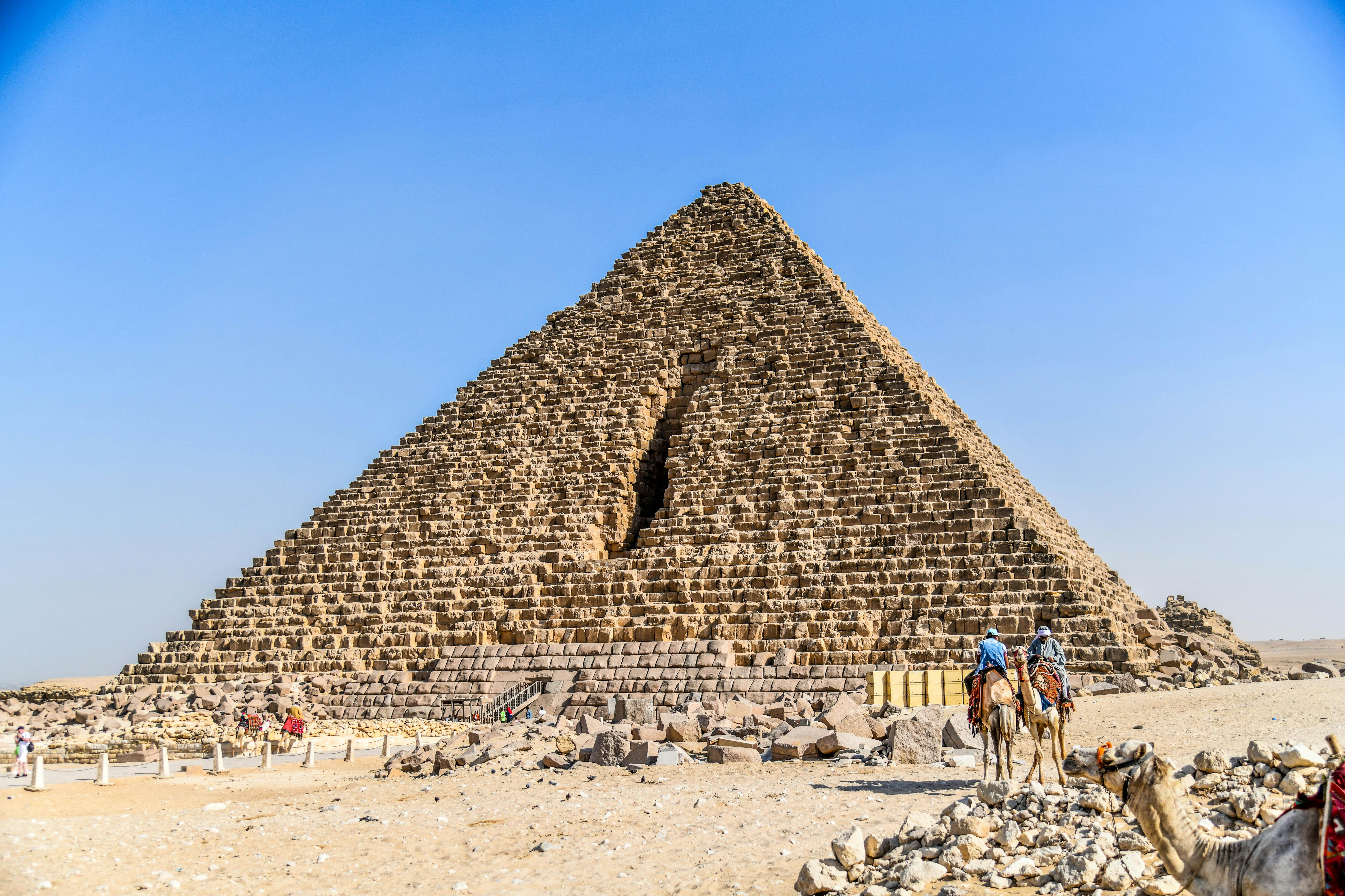 Tourists ride camels near the Pyramid of Khafre in Giza, Egypt, under a clear blue sky.