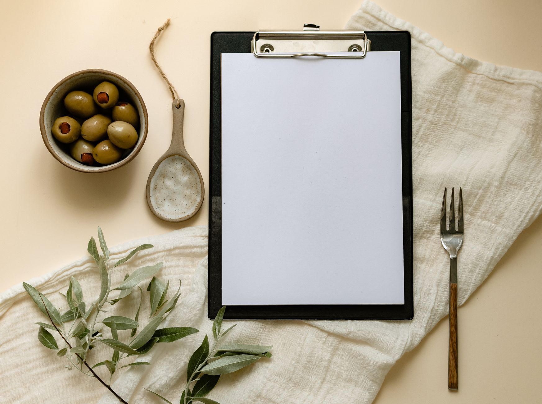 Flat lay of olives, a clipboard, and kitchen items creating a minimalist scene.