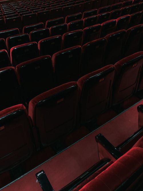 Free Rows of empty red velvet seats in a dimly lit theater, creating a dramatic atmosphere. Stock Photo
